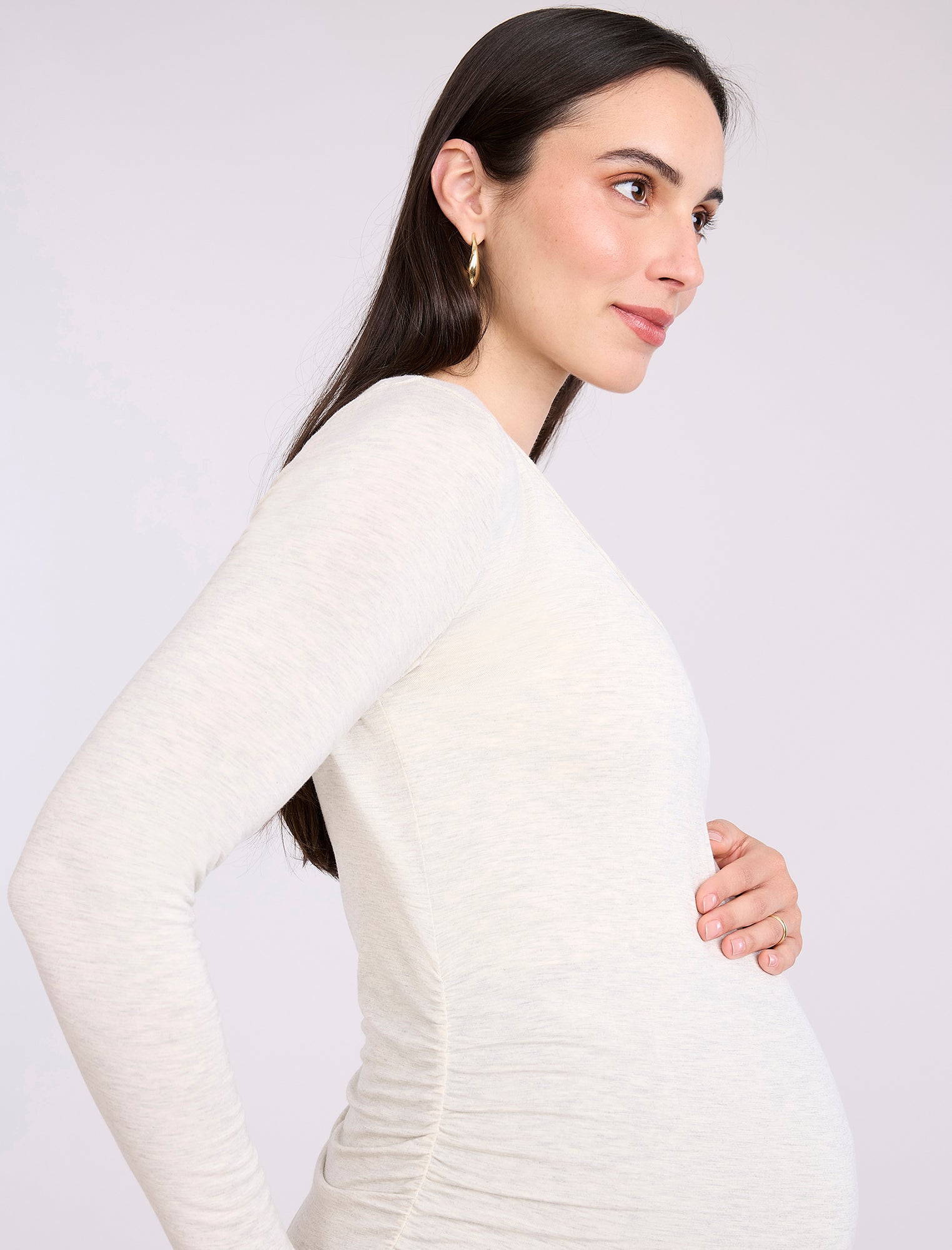 Pregnant woman wearing an off-white long-sleeve maternity top against a plain background