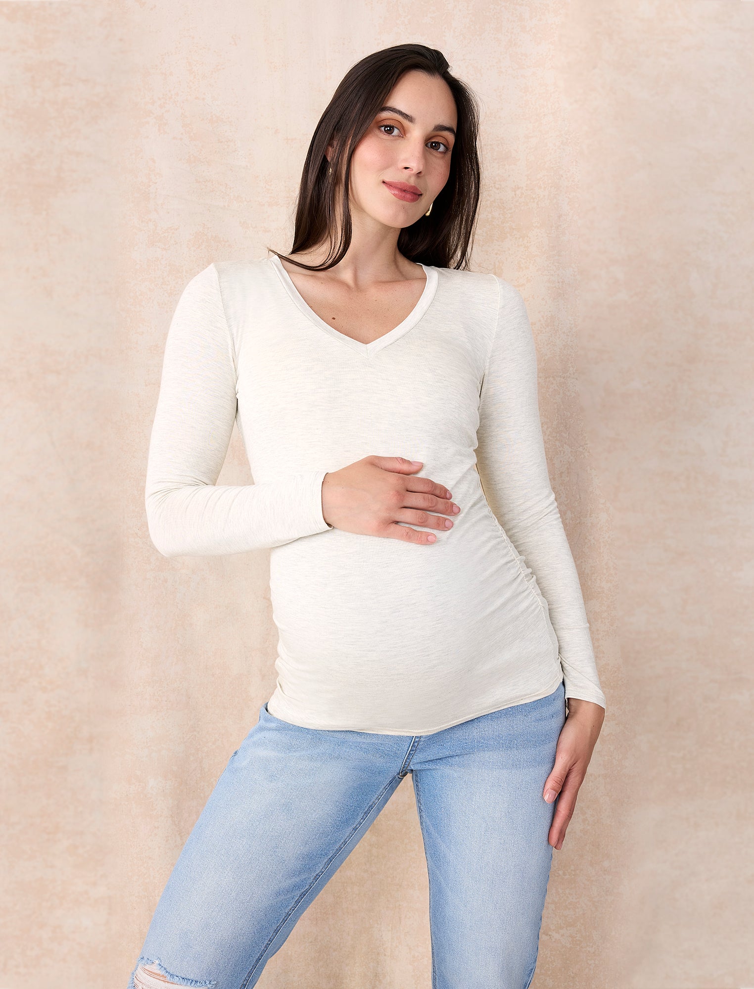 Pregnant woman wearing an off-white long-sleeve maternity top against a plain background