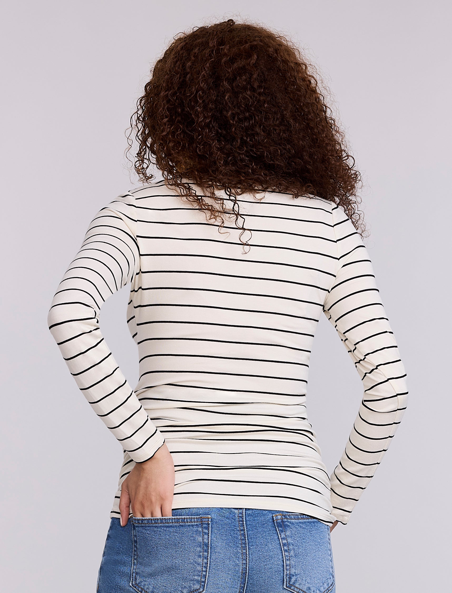 Pregnant woman wearing a white and black striped long-sleeve maternity top against a plain background