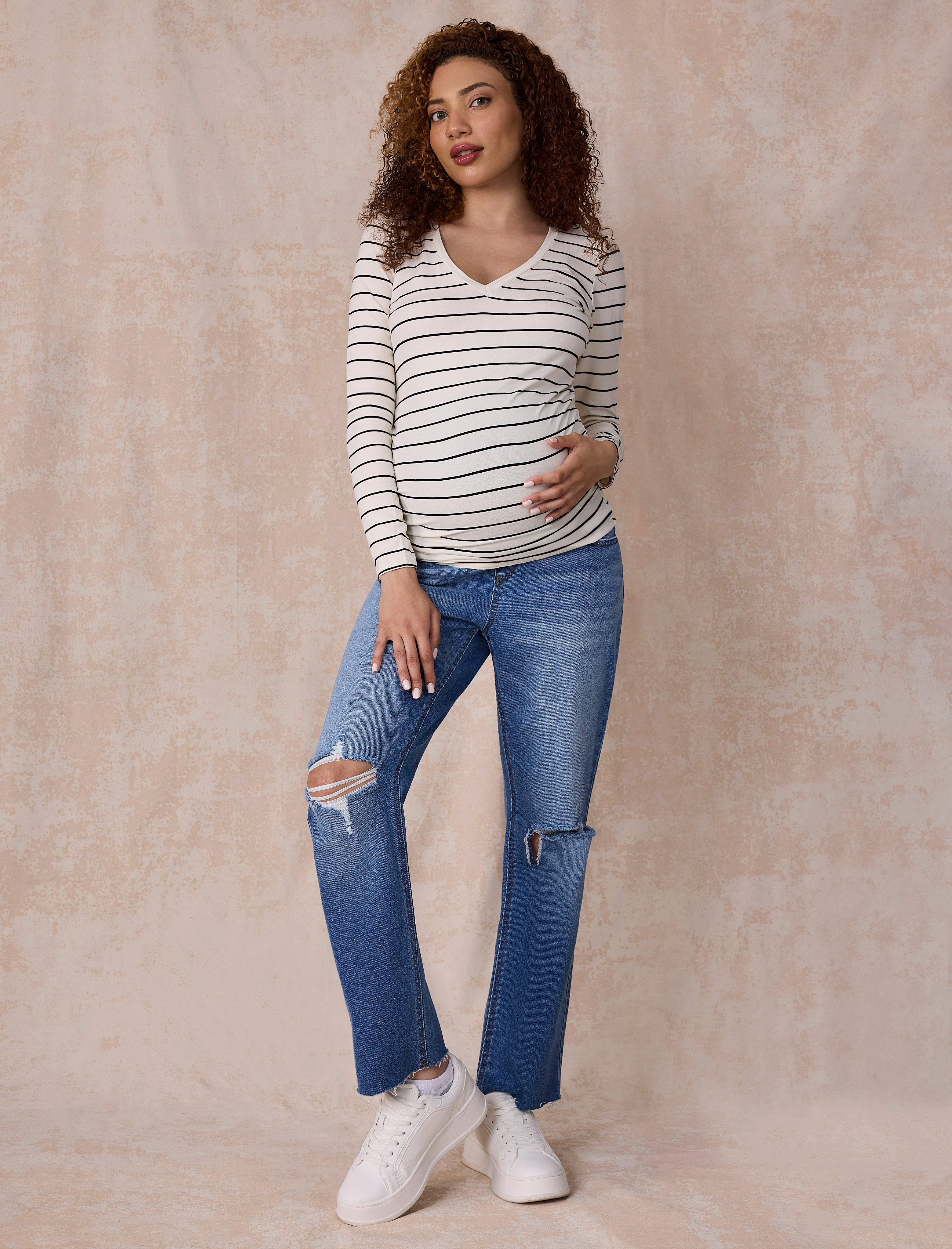 Pregnant woman wearing a white and black striped long-sleeve maternity top against a plain background