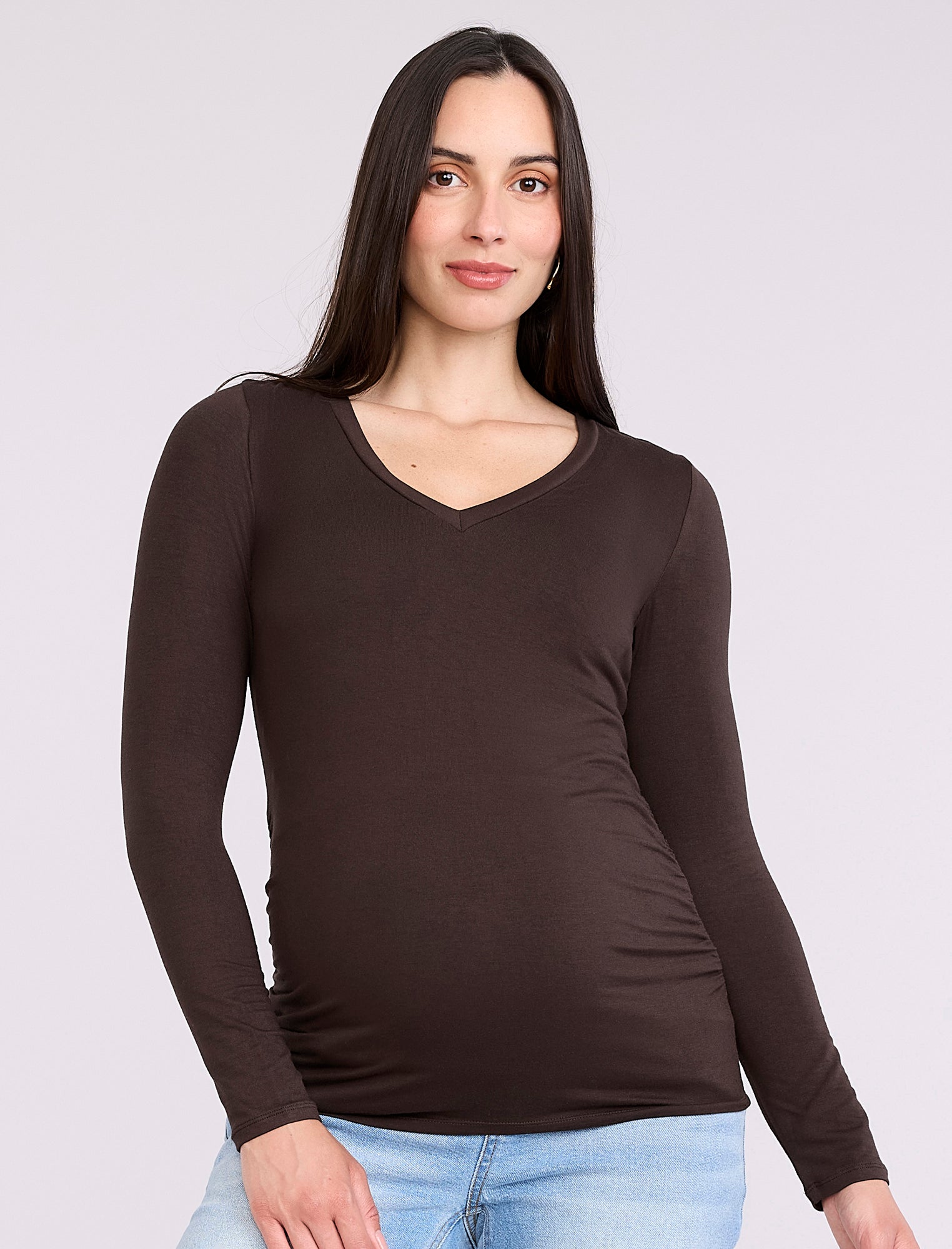 Pregnant woman wearing a brown long-sleeve maternity top against a plain background