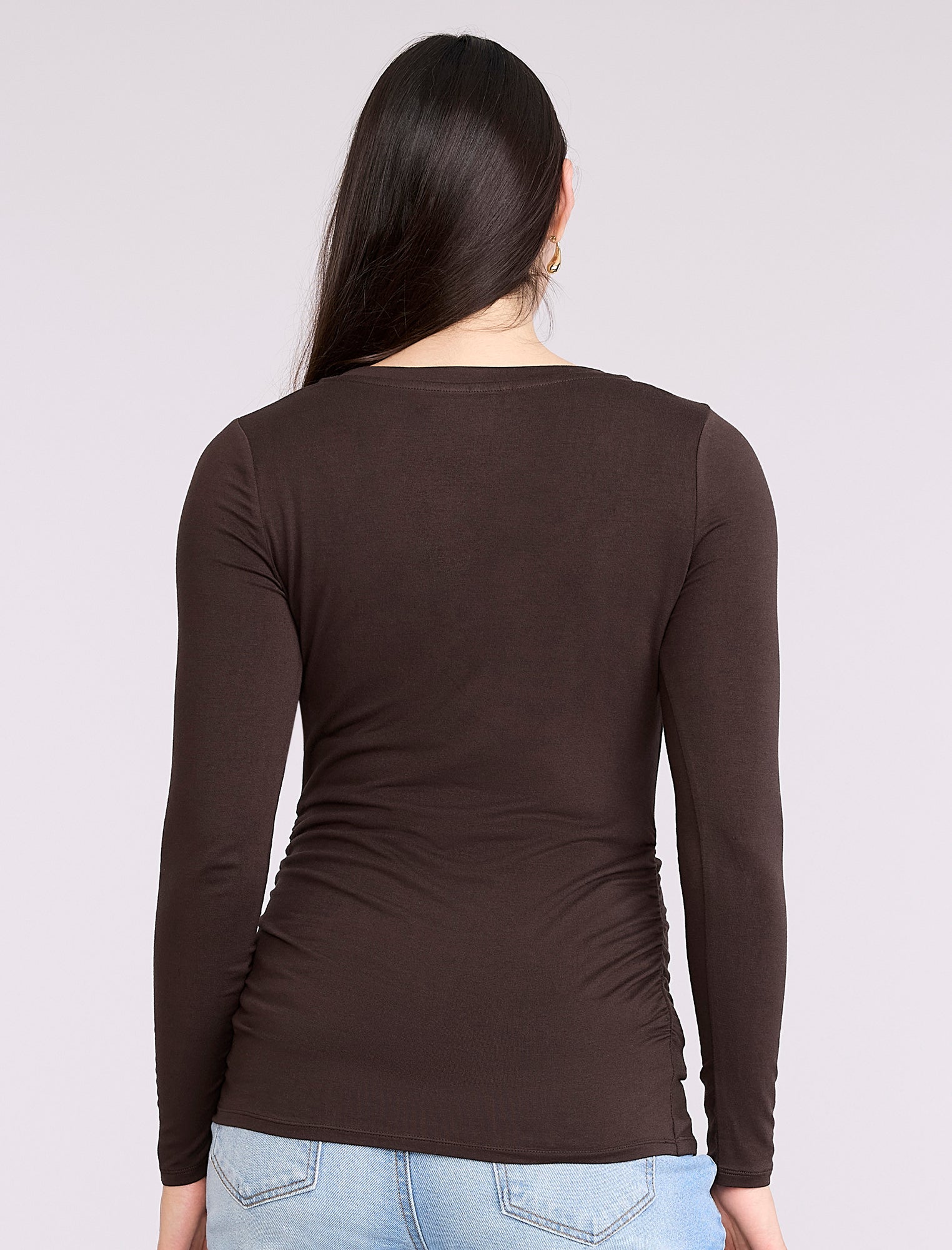 Pregnant woman wearing a brown long-sleeve maternity top against a plain background