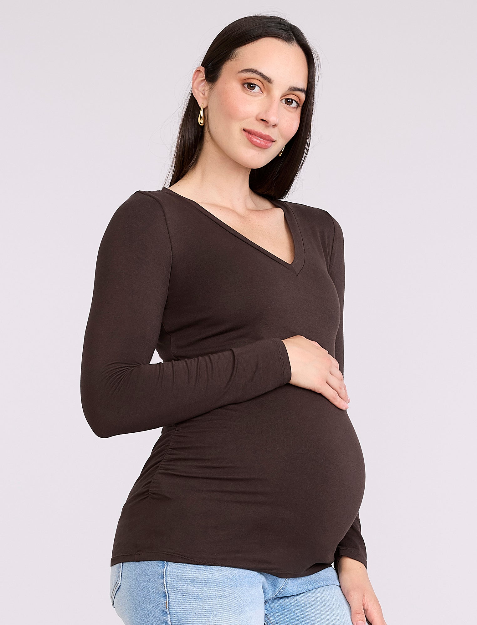 Pregnant woman wearing a brown long-sleeve maternity top against a plain background