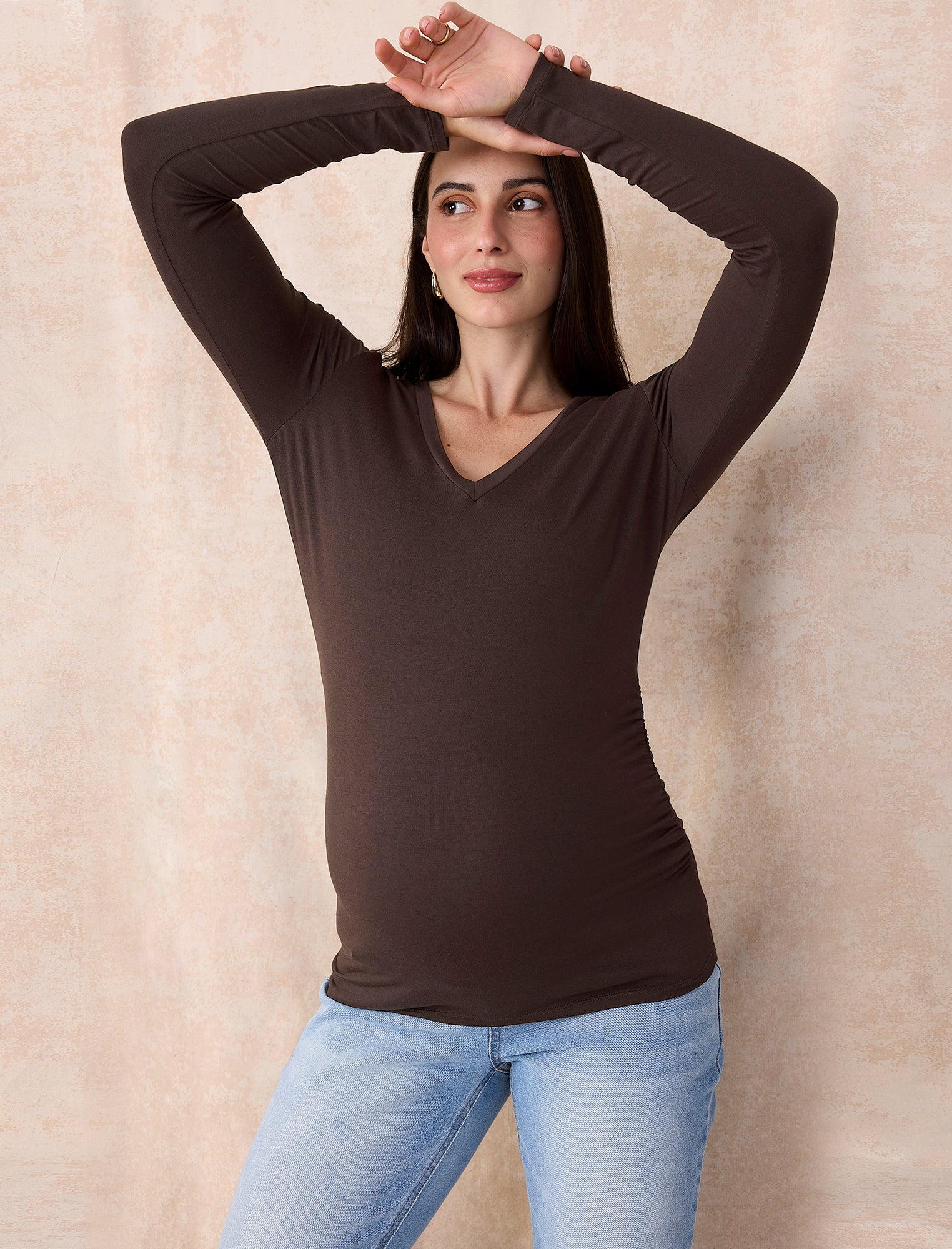 Pregnant woman wearing a brown long-sleeve maternity top against a plain background
