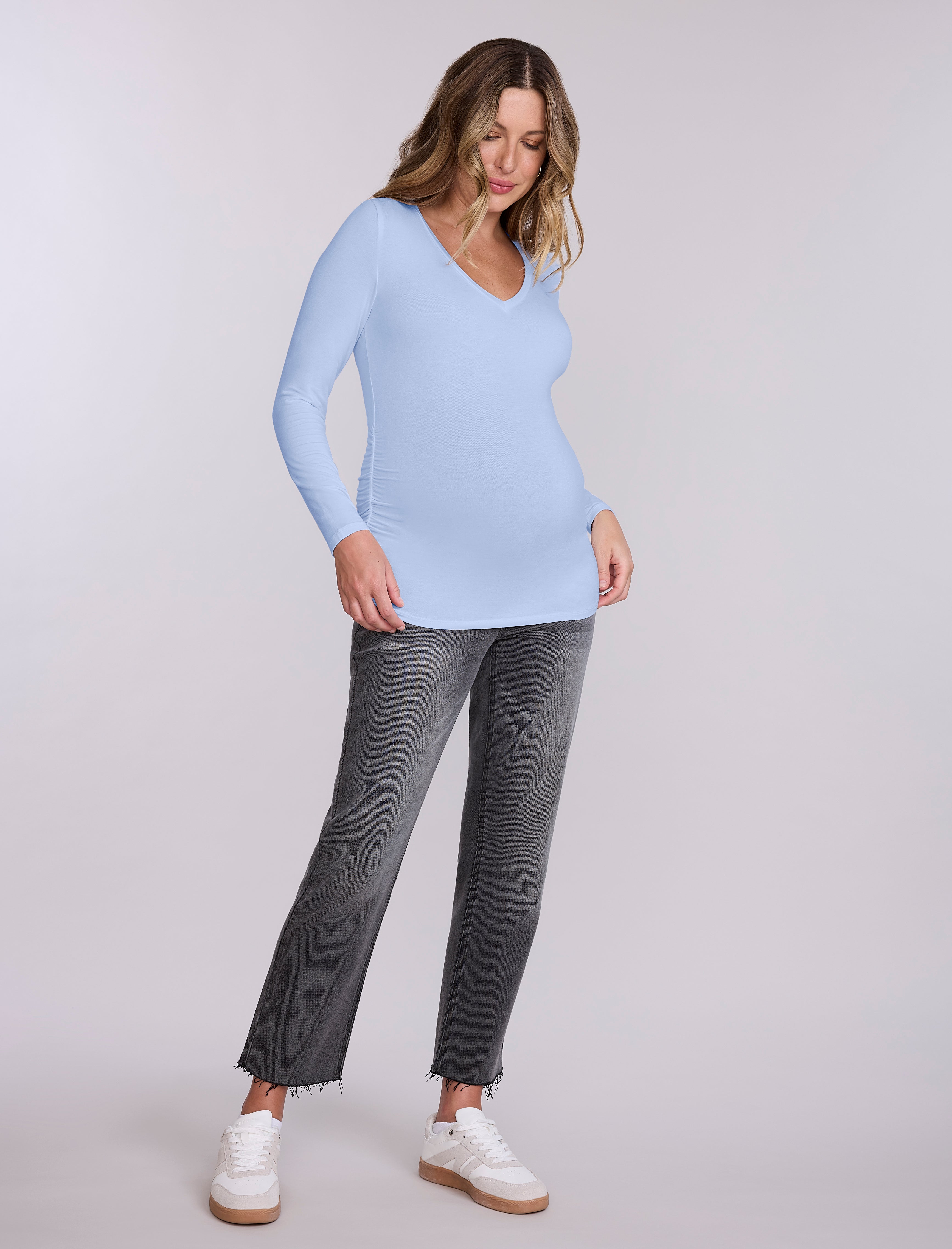 Pregnant woman wearing a light blue long-sleeve top against a plain background