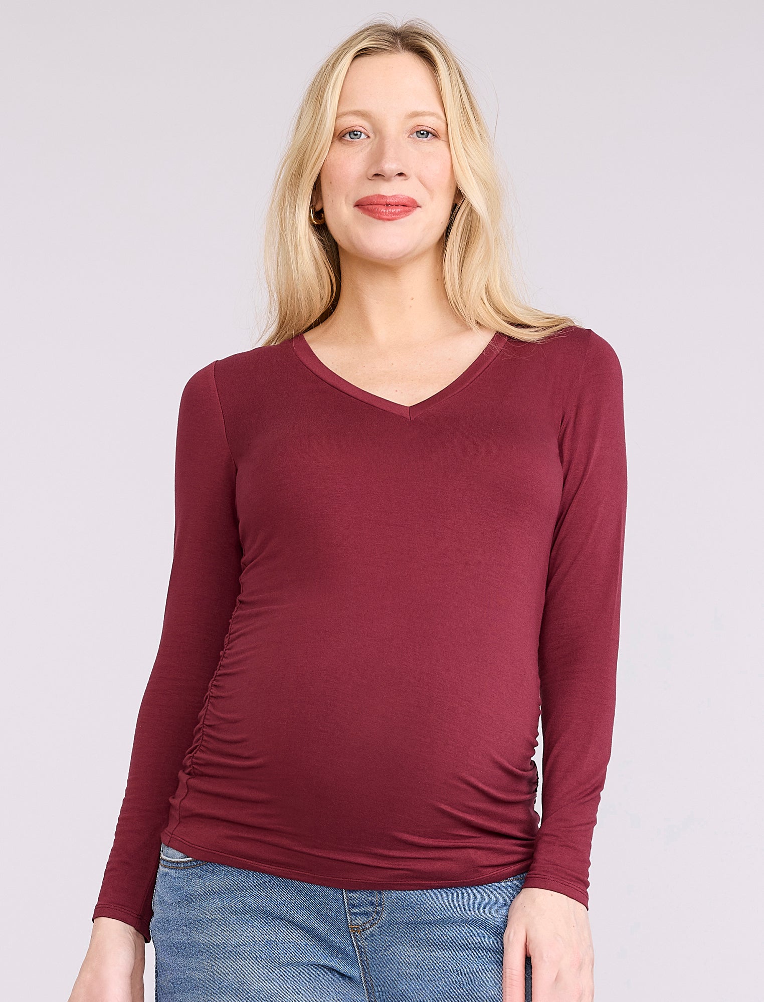 Pregnant woman wearing a maroon long-sleeve top against a plain background