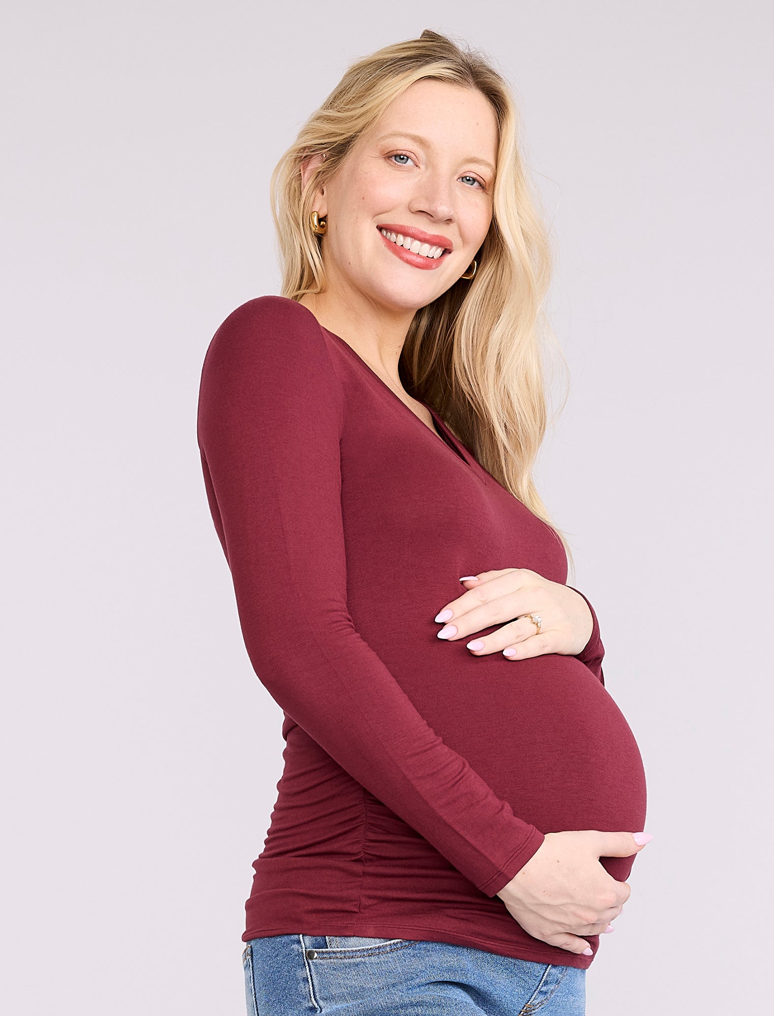 Pregnant woman wearing a maroon long-sleeve top against a plain background