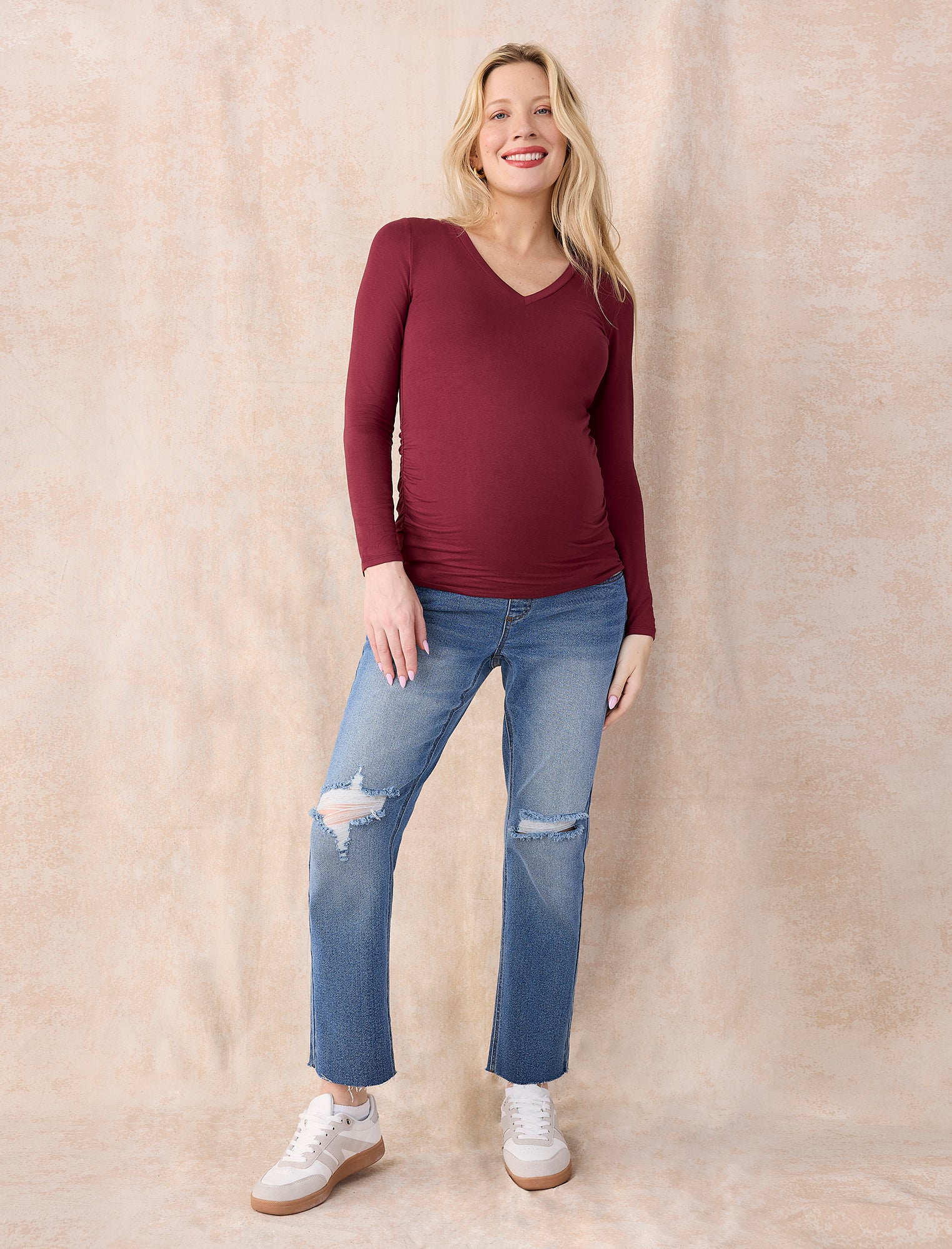 Pregnant woman wearing a maroon long-sleeve top against a plain background