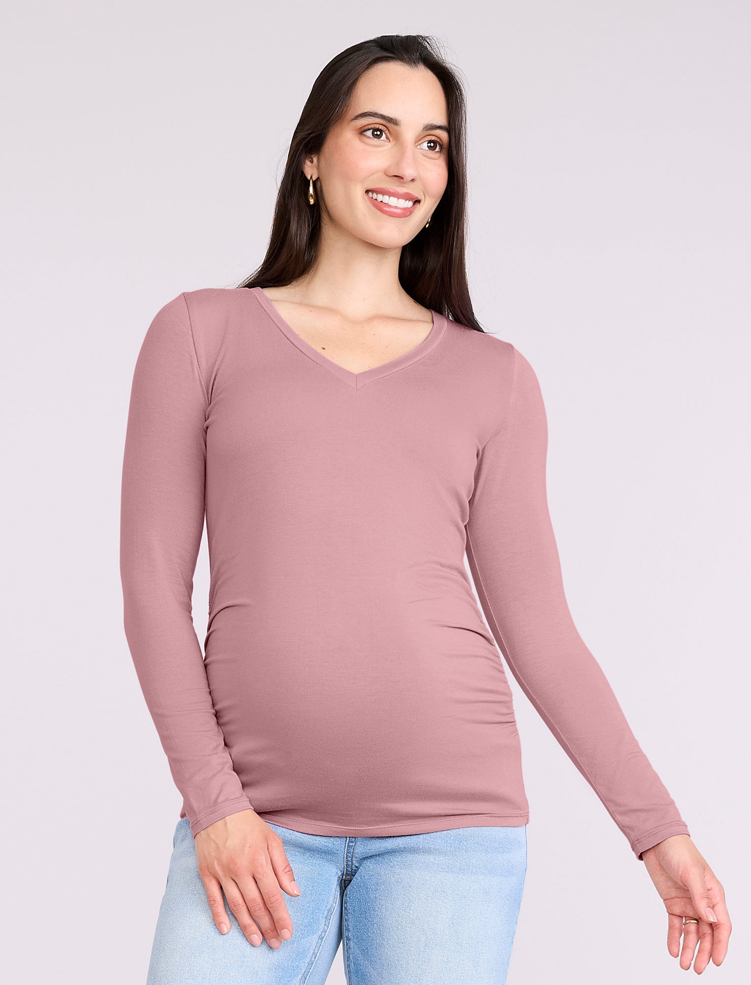 Pregnant woman wearing a mauve long-sleeve top and light blue jeans on a white background