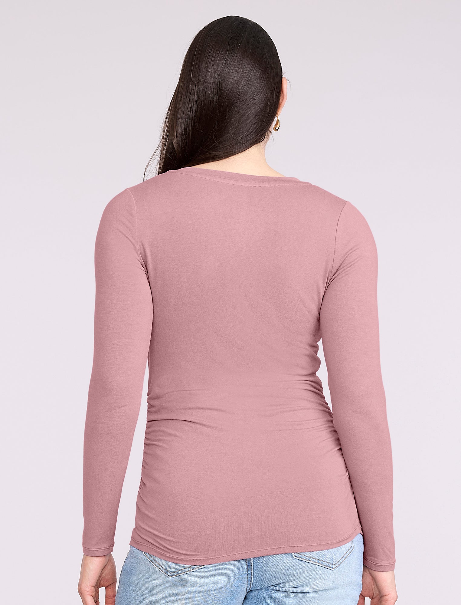 Pregnant woman wearing a mauve long-sleeve top and light blue jeans on a white background