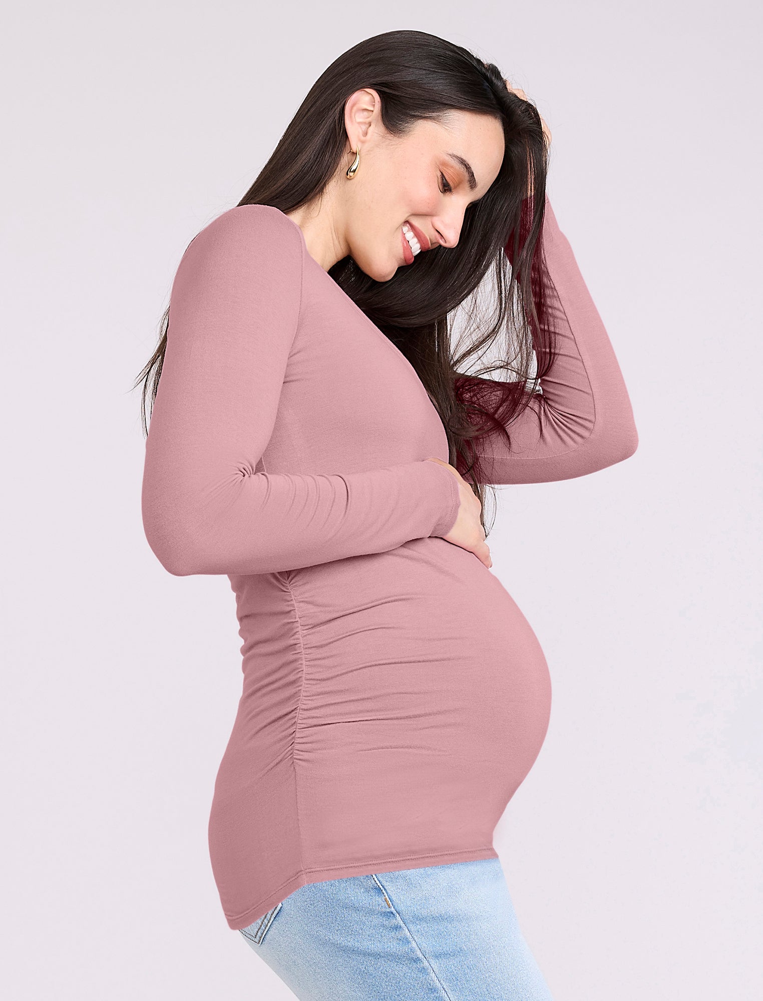 Pregnant woman wearing a mauve long-sleeve top and light blue jeans on a white background