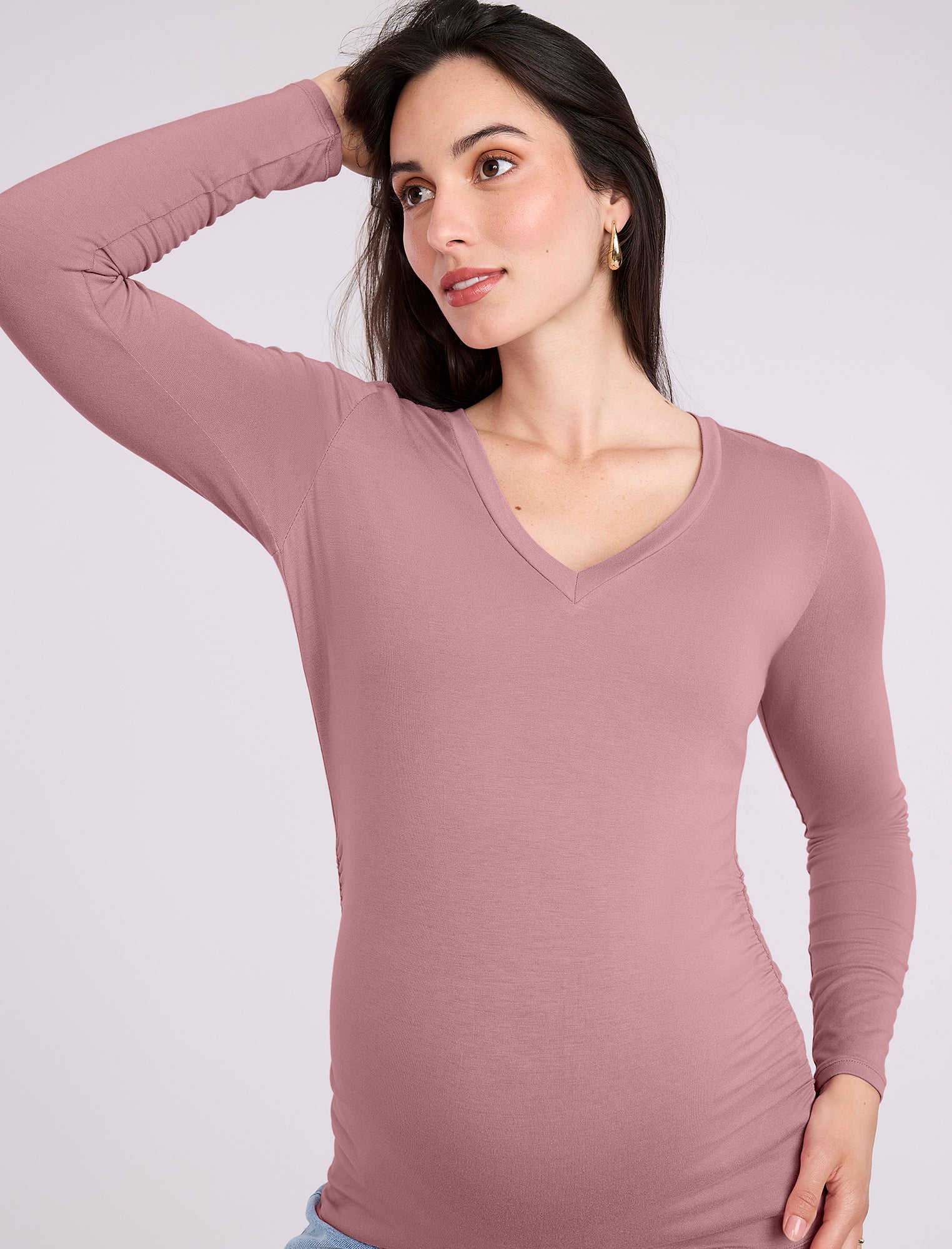Pregnant woman wearing a mauve long-sleeve top on a white background