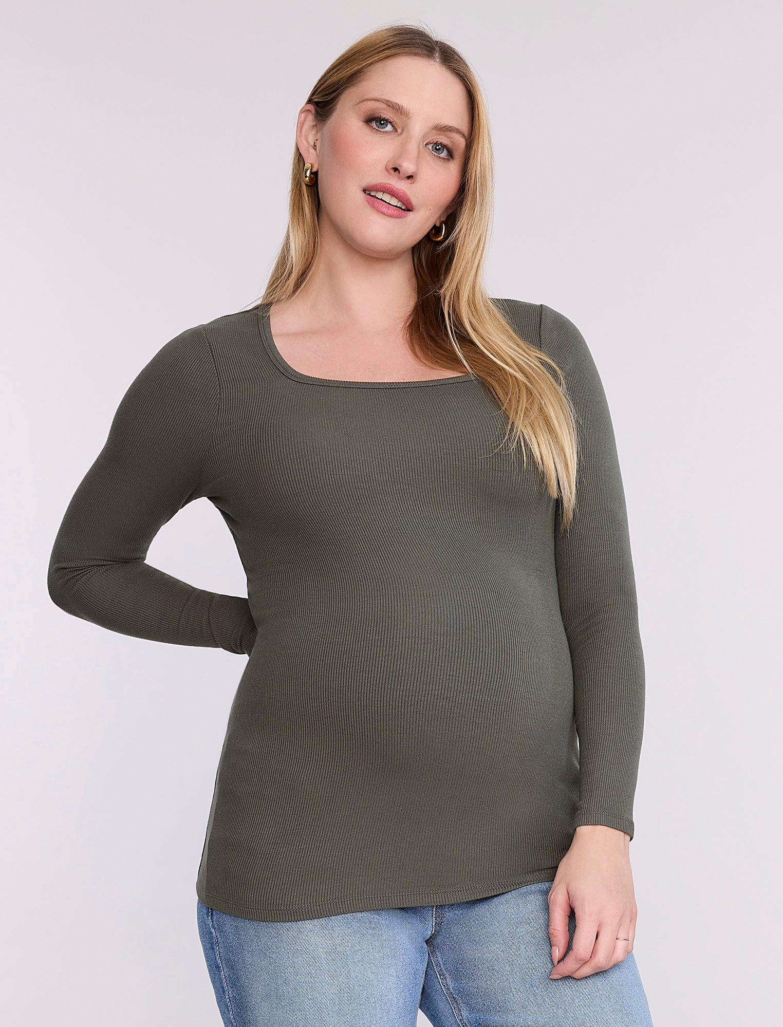 Pregnant woman wearing a green long-sleeve top against a white background