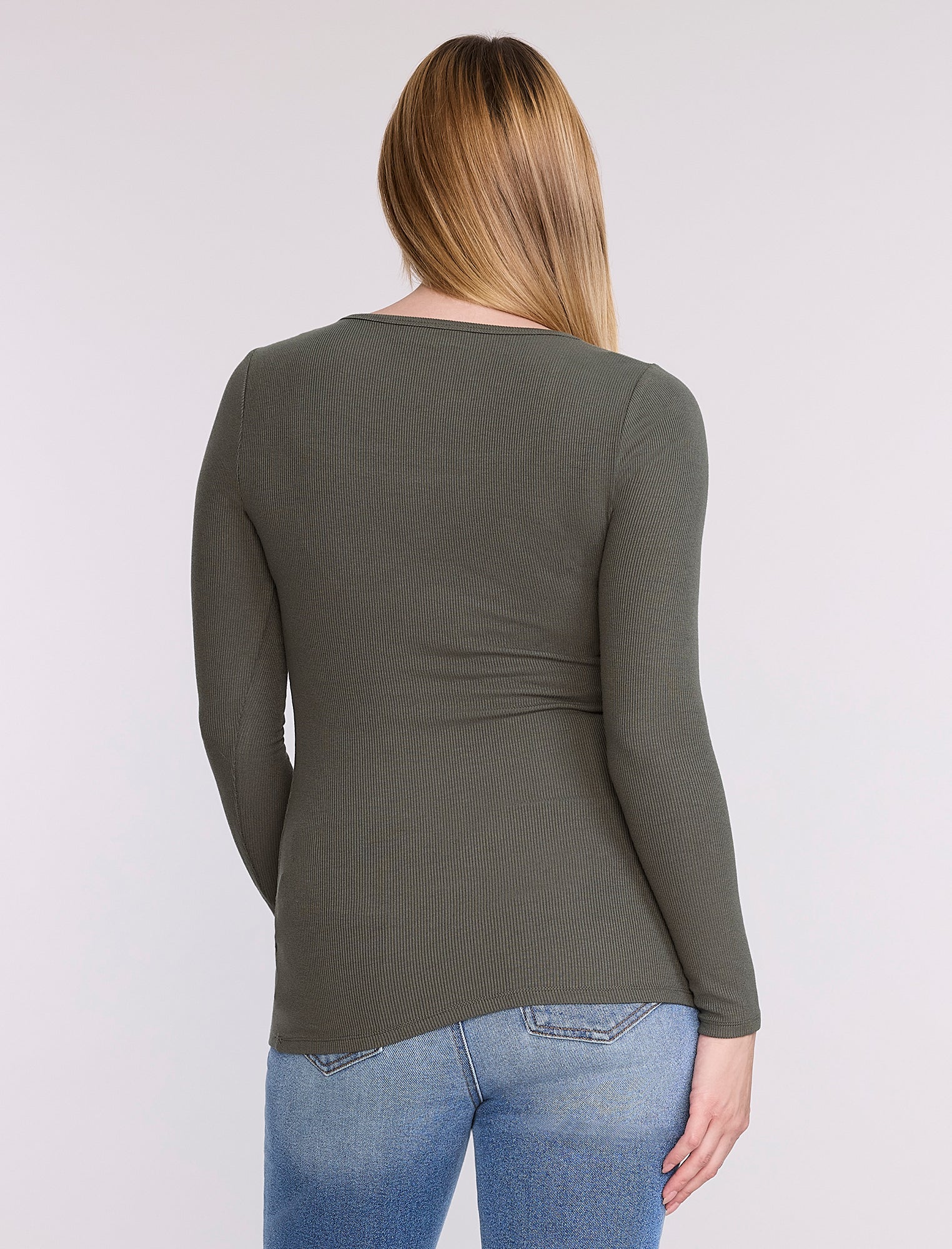 Pregnant woman wearing a green long-sleeve top against a white background