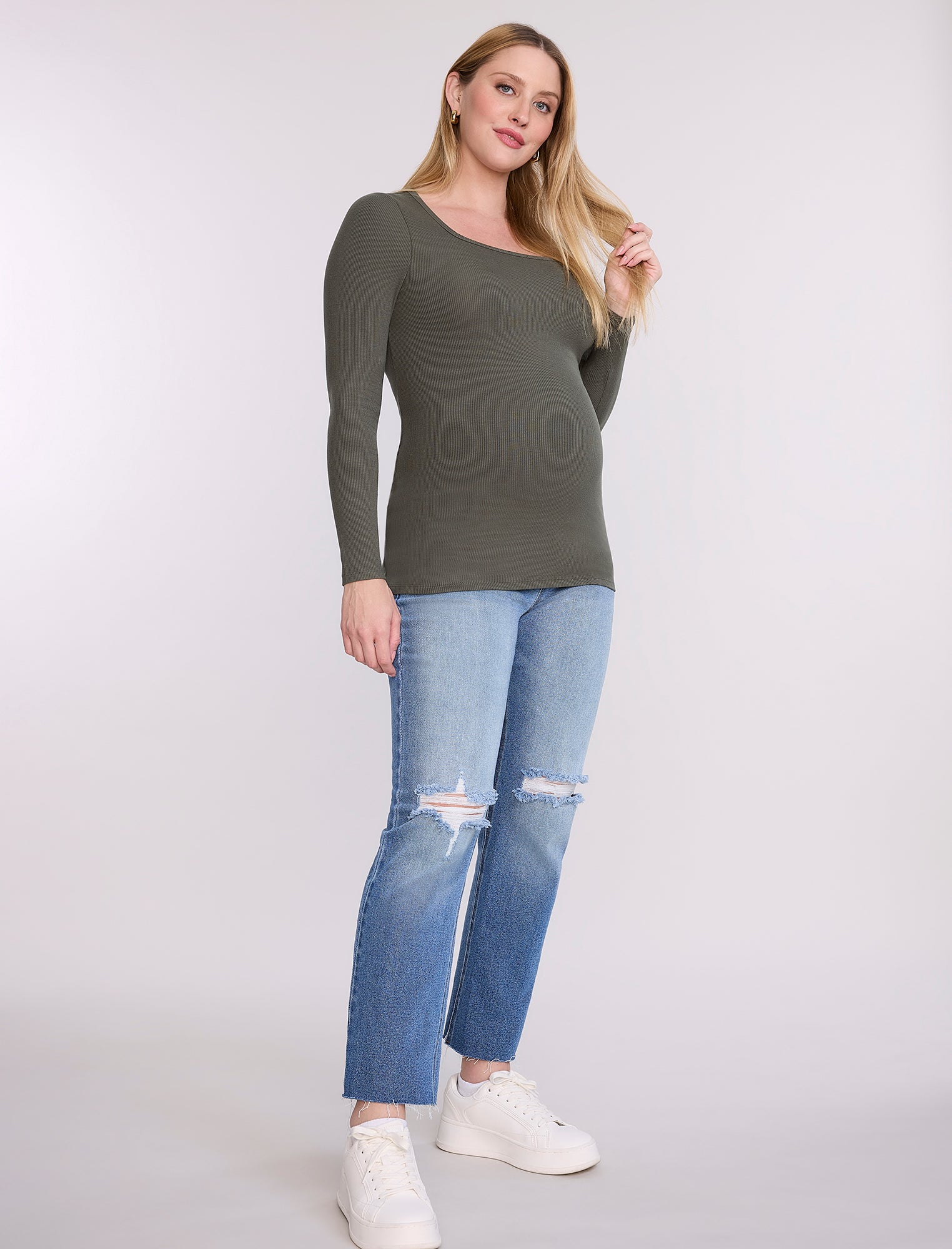 Pregnant woman wearing a green long-sleeve top against a white background