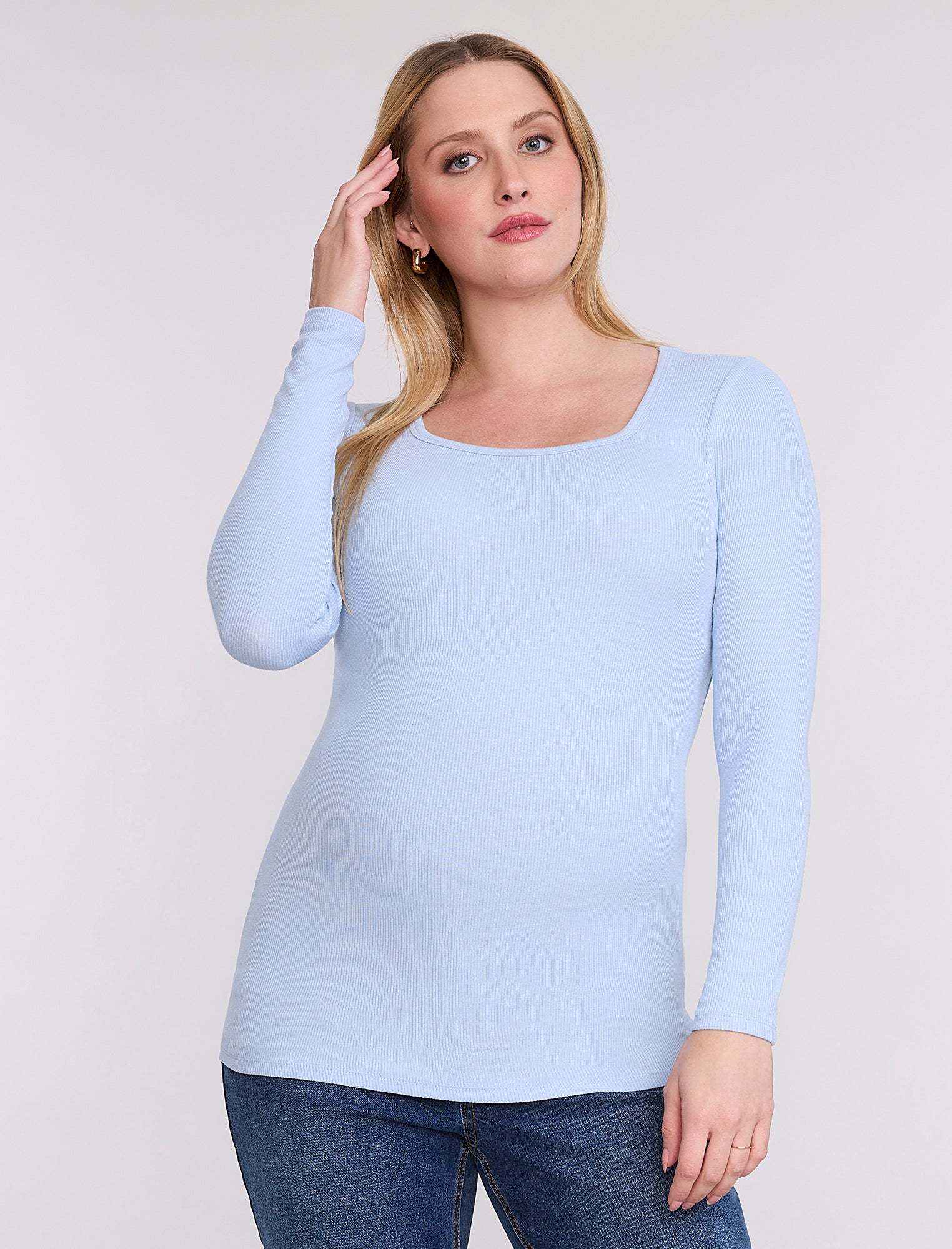 Pregnant woman wearing a light blue long-sleeve top against a white background