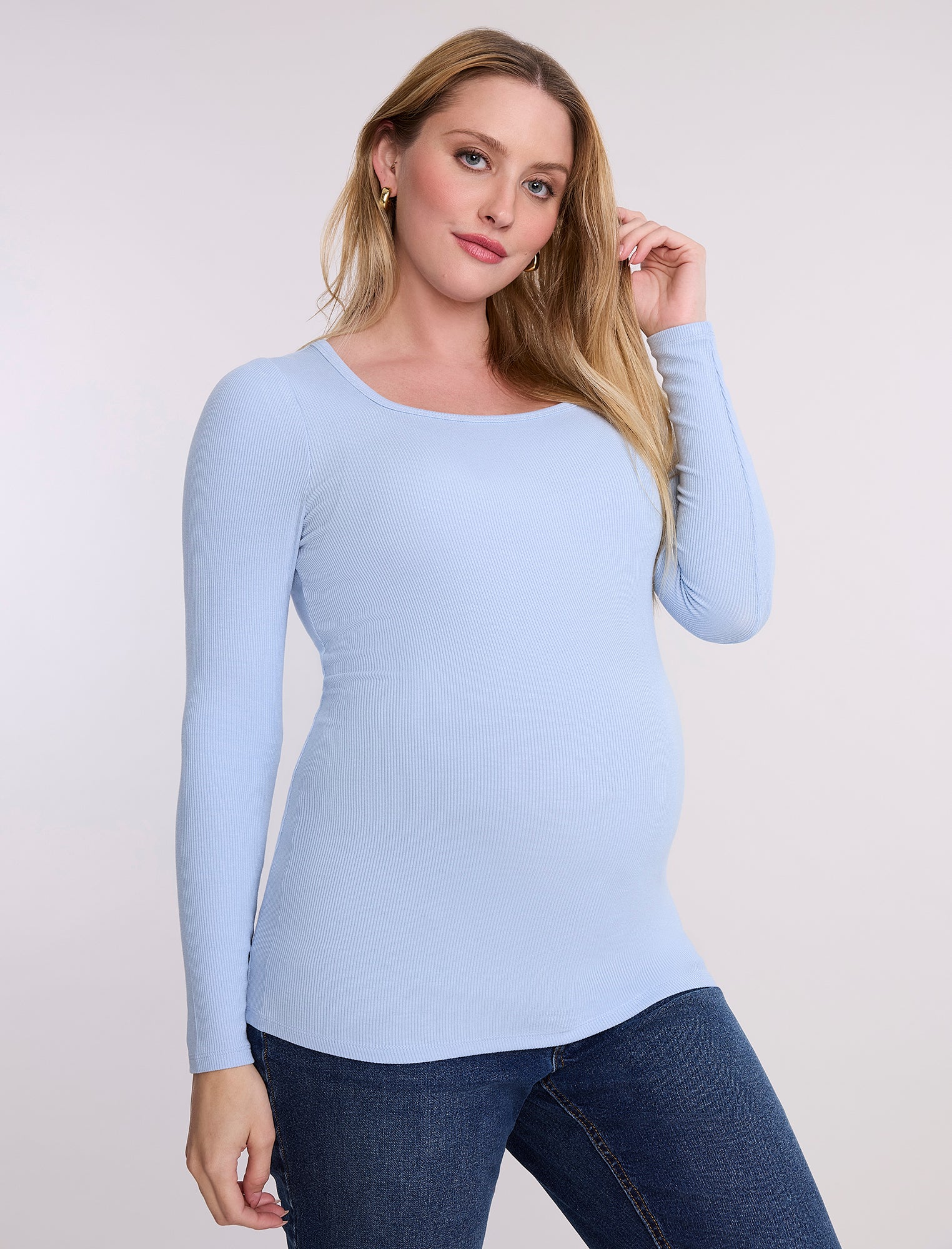 Pregnant woman wearing a light blue long-sleeve top against a white background