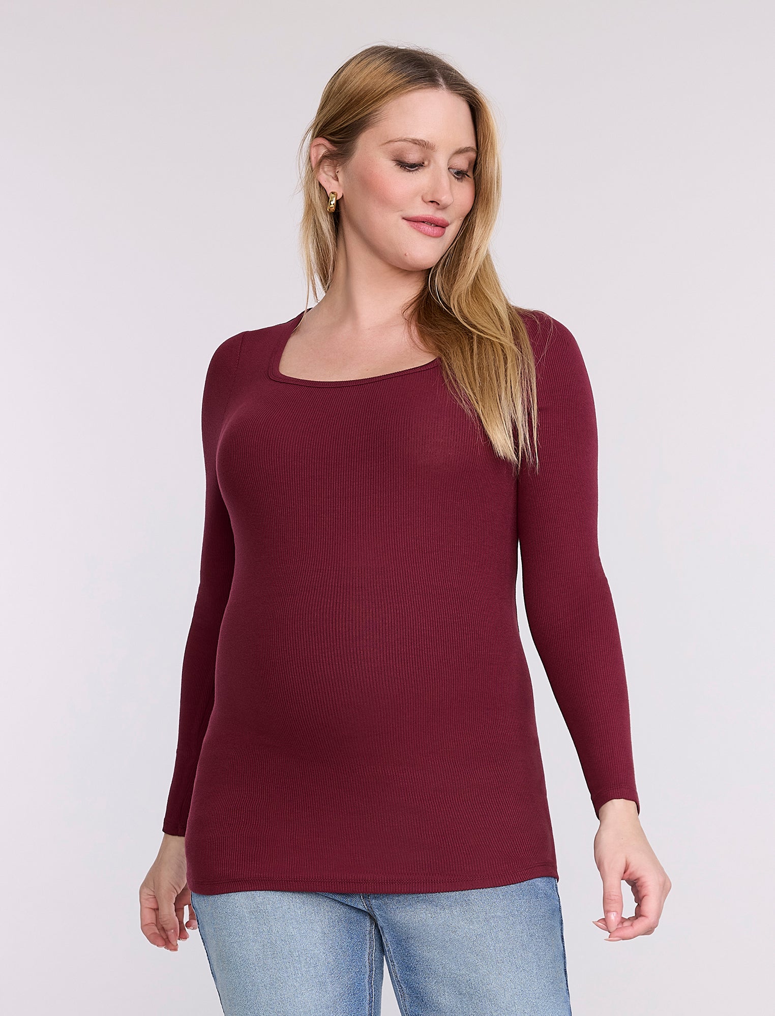 Pregnant woman wearing a burgundy long-sleeve top against a white background