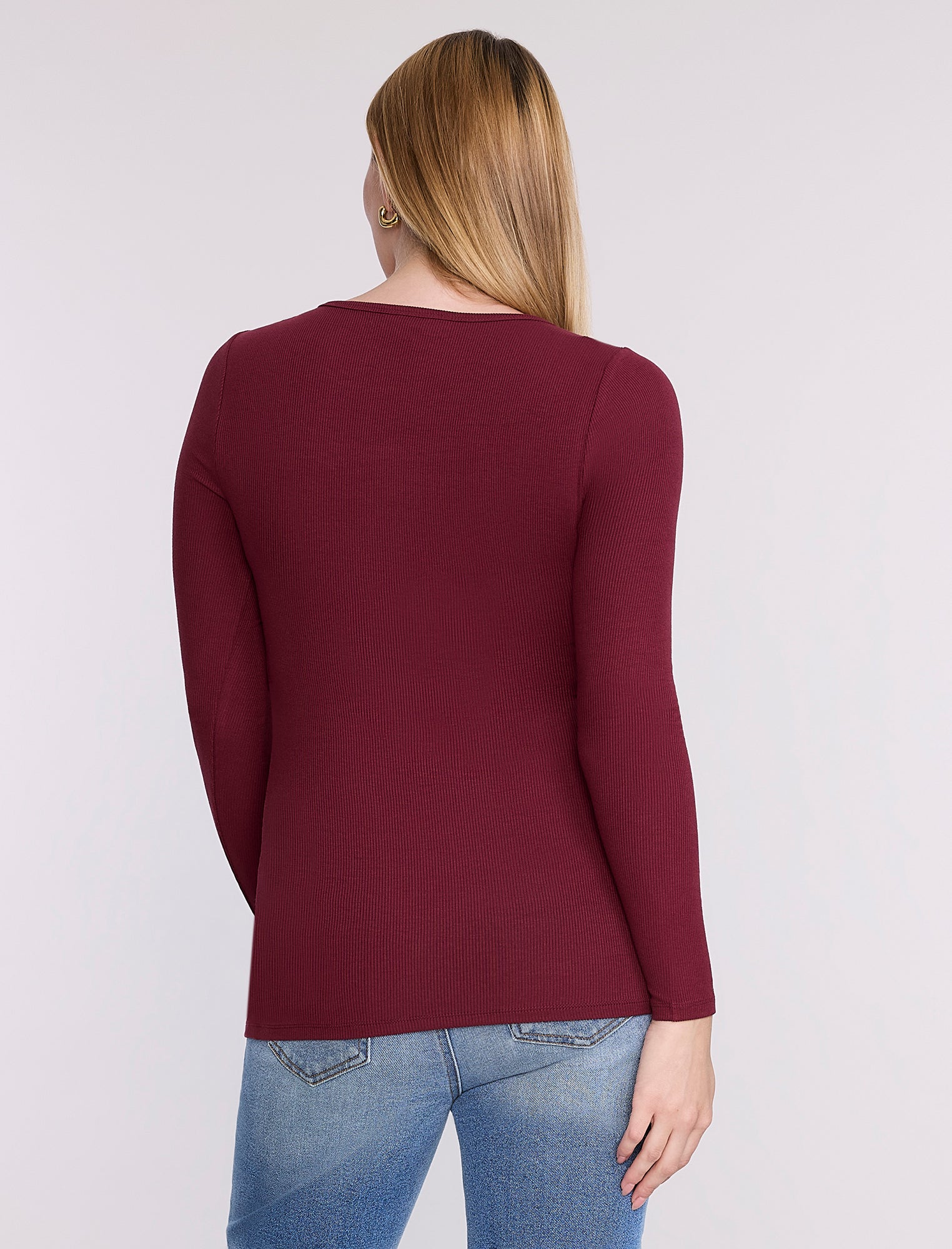 Pregnant woman wearing a burgundy long-sleeve top against a white background