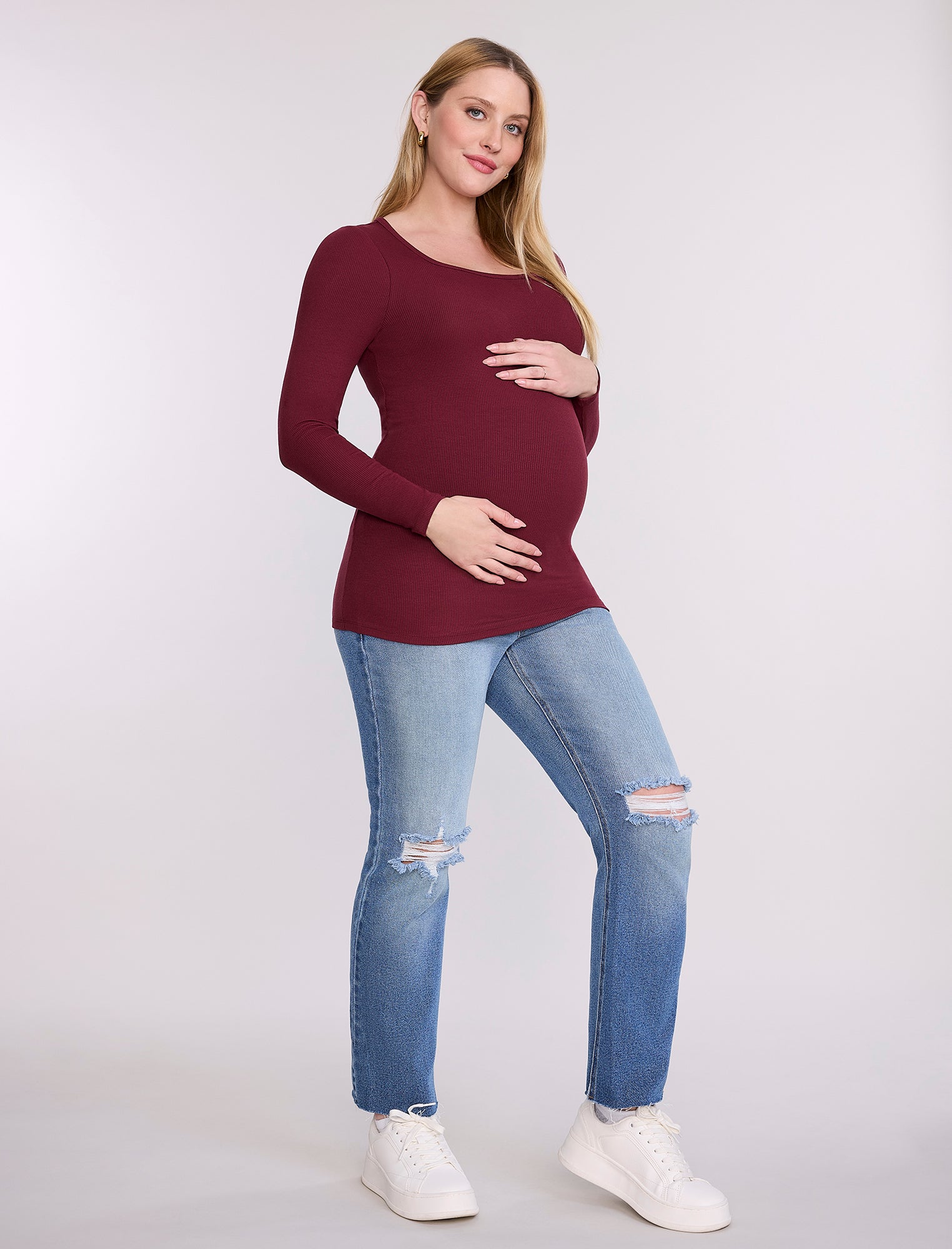 Pregnant woman wearing a burgundy long-sleeve top against a white background