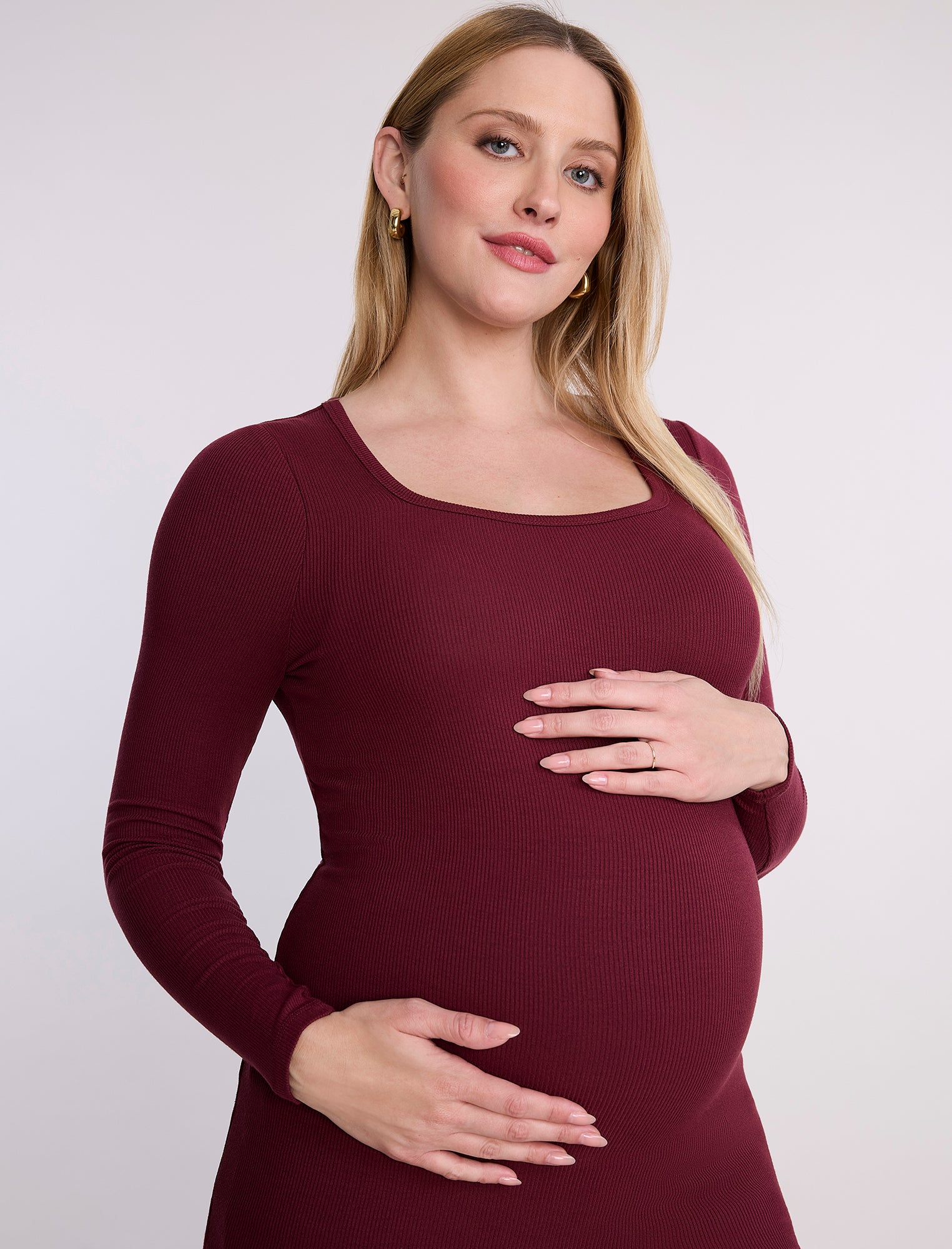 Pregnant woman wearing a burgundy long-sleeve top against a white background