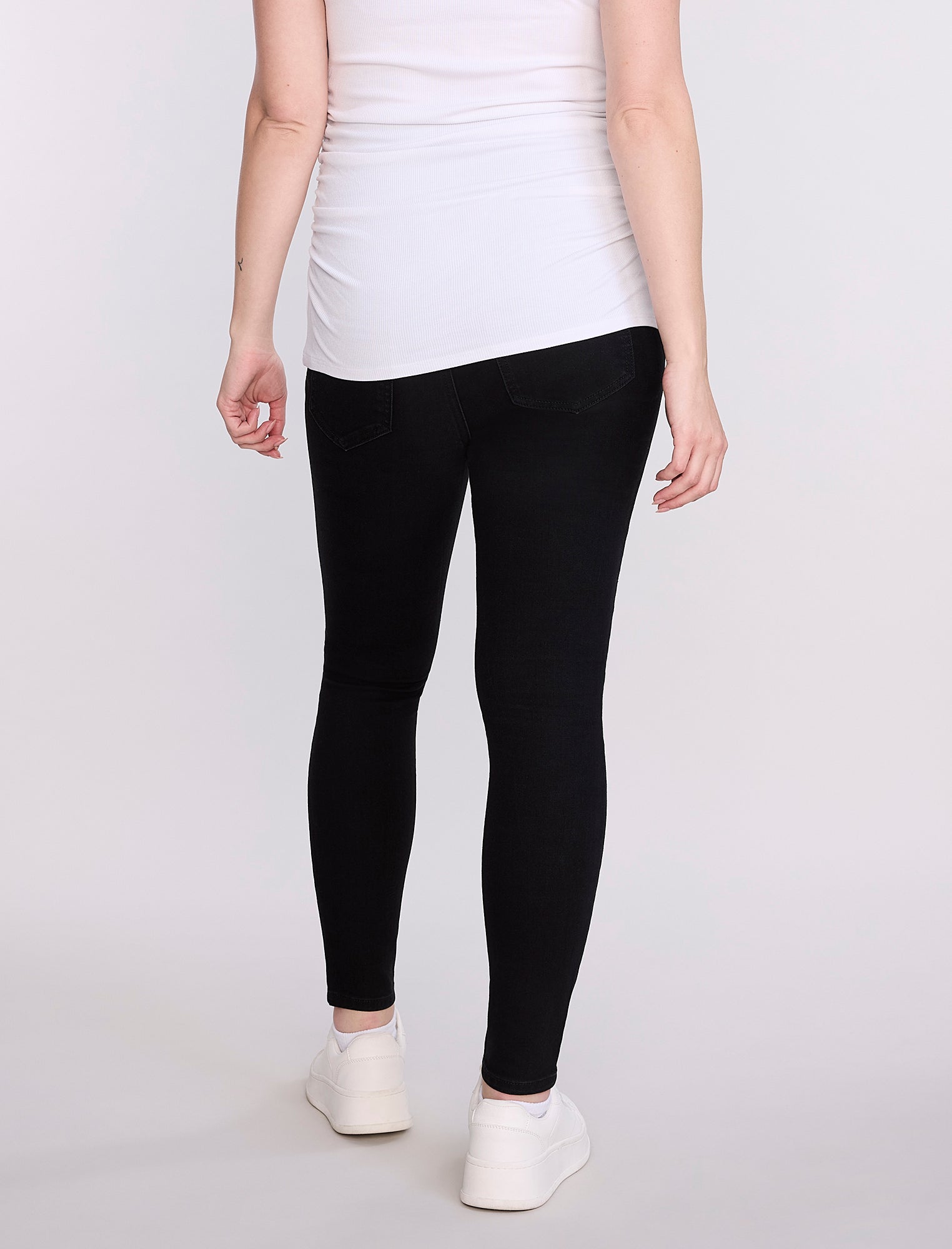 Pregnant woman wearing black leggings and a white top on a plain background