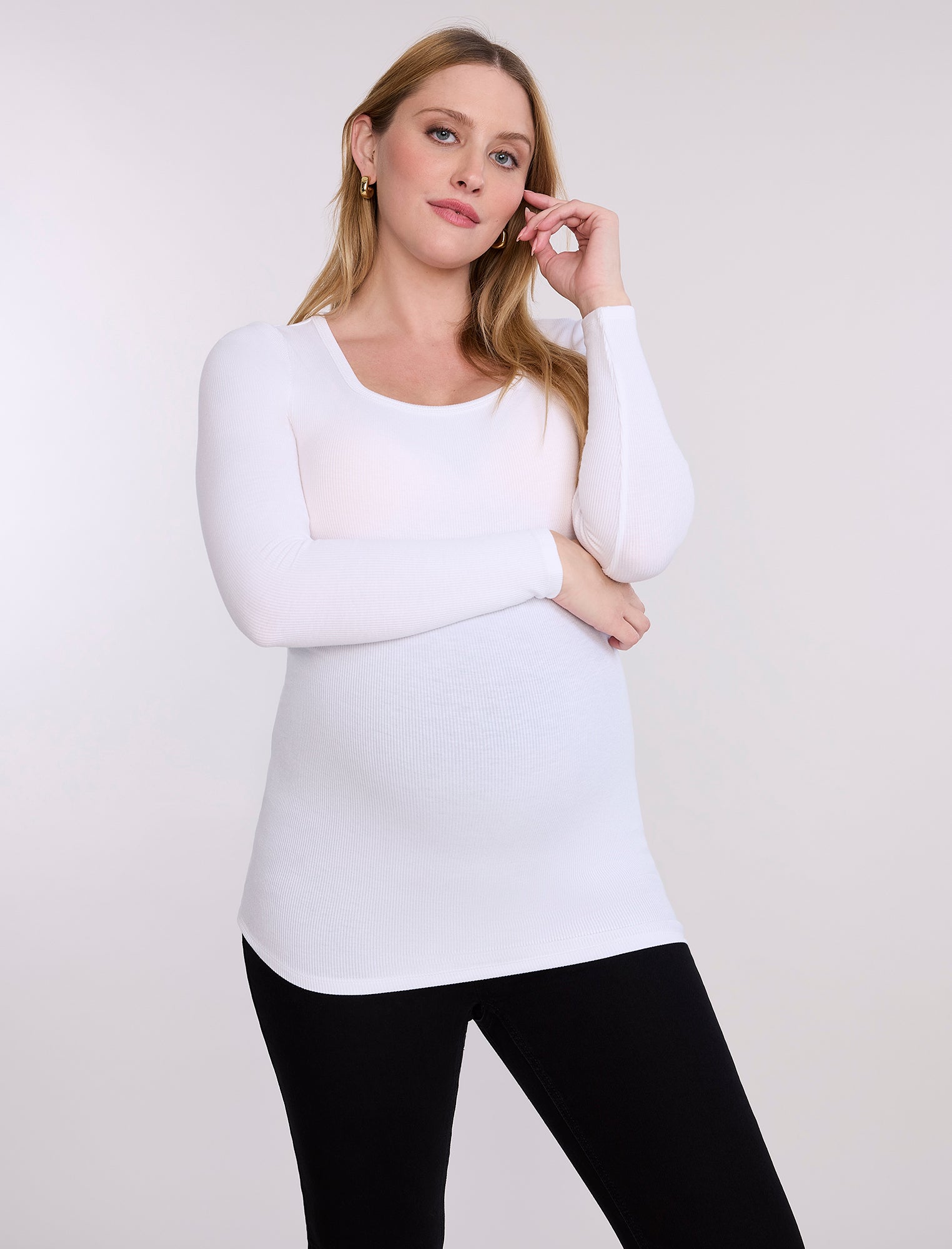 Pregnant woman wearing black leggings and a white top on a plain background
