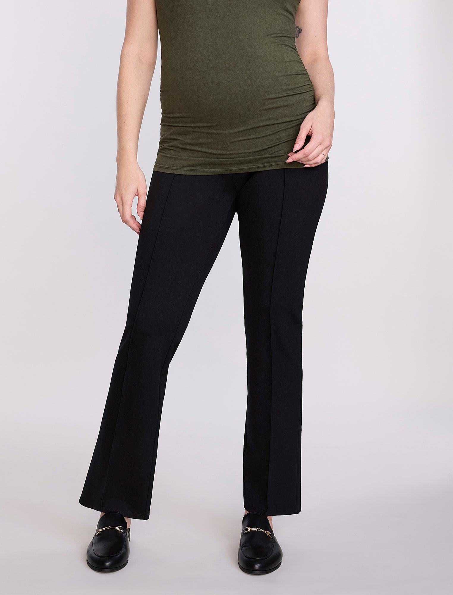 Pregnant woman wearing a green top and black pants on a white background