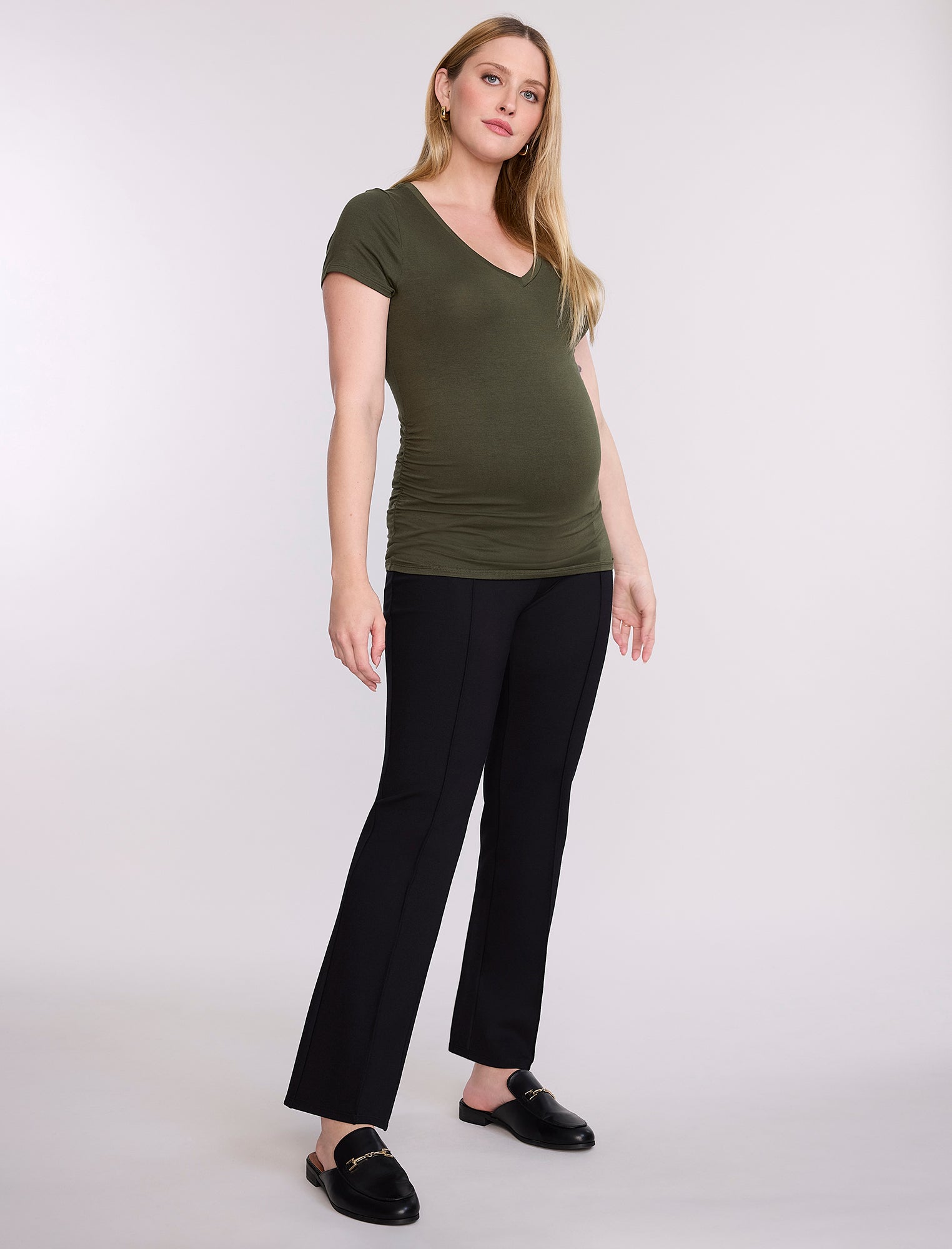 Pregnant woman wearing a green top and black pants on a white background