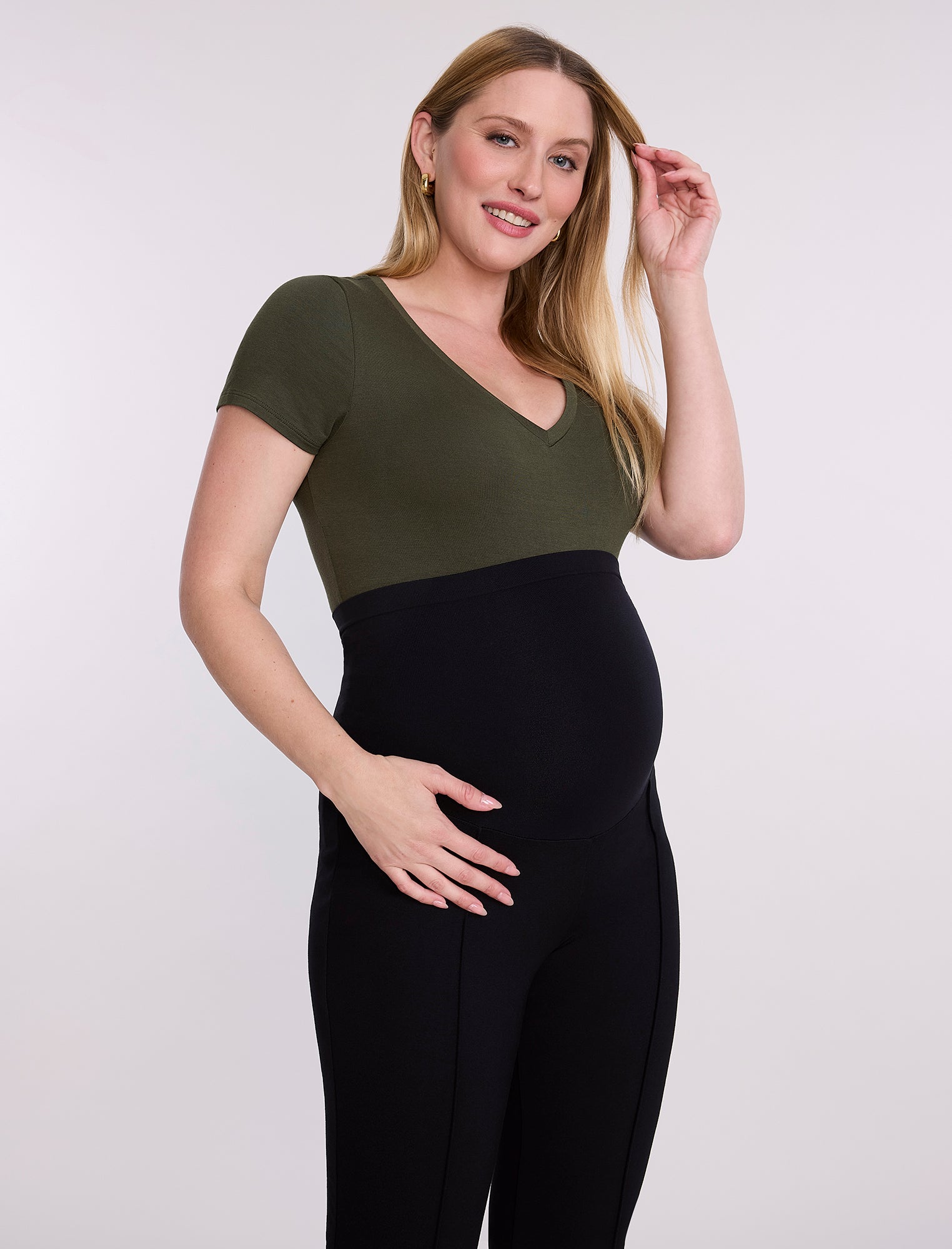 Pregnant woman wearing a green top and black pants on a white background