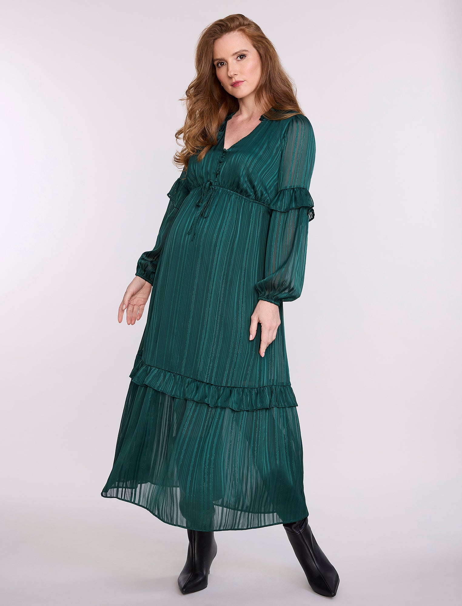 Pregnant woman wearing a green dress with long sleeves and ruffled layers on a white background