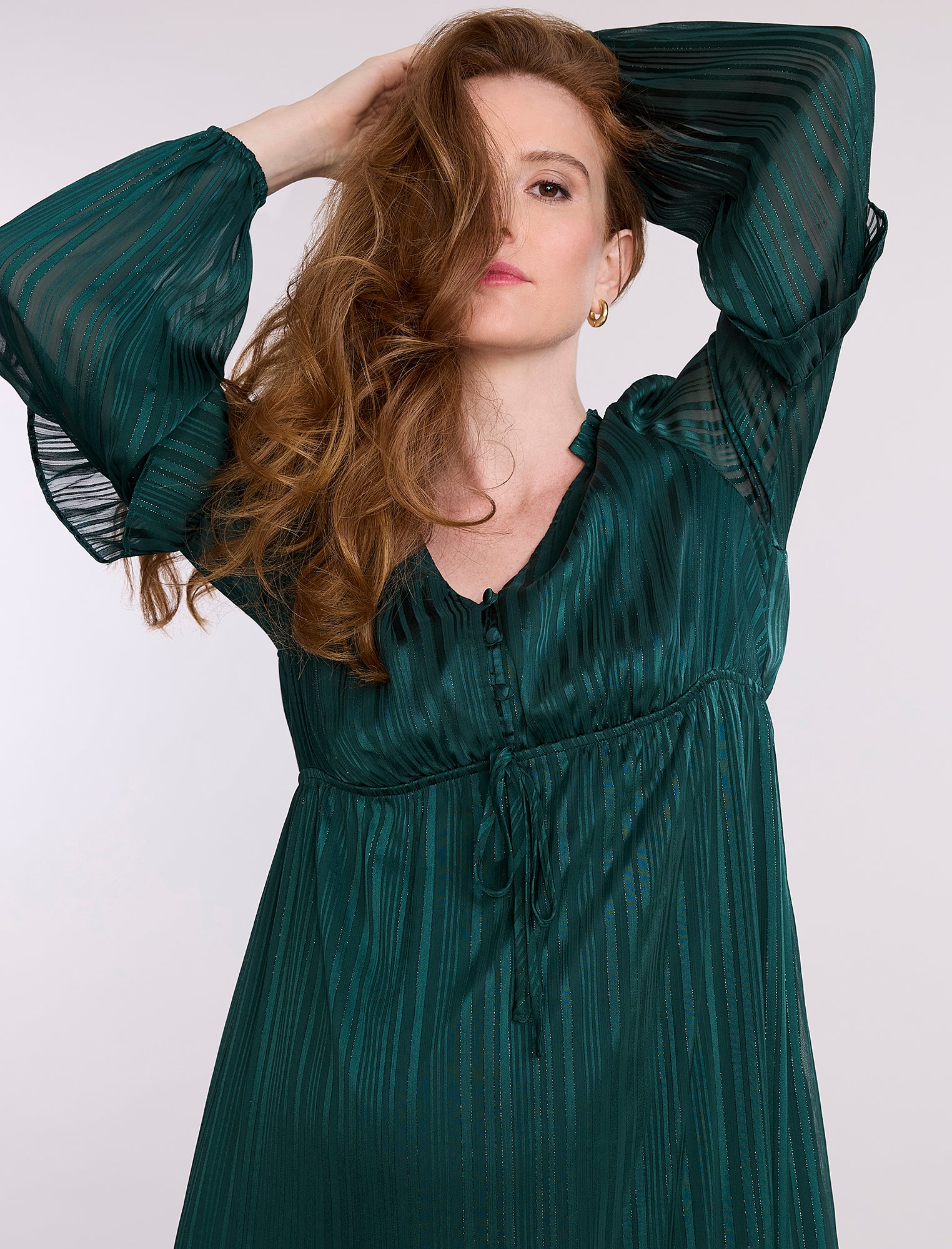 Pregnant woman wearing a green dress with long sleeves and ruffled layers on a white background