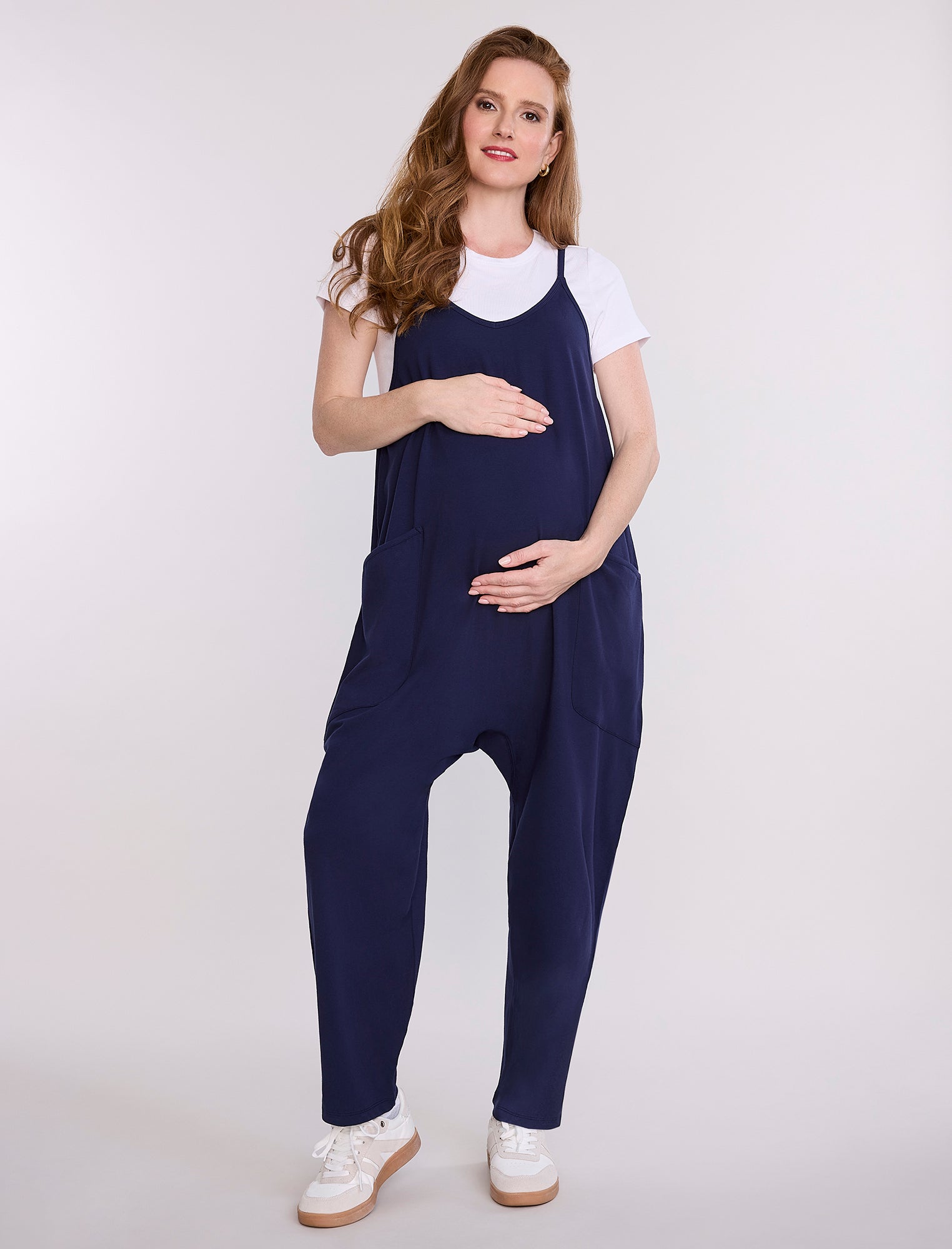 Pregnant woman wearing a navy blue jumpsuit over a white shirt on a light gray background