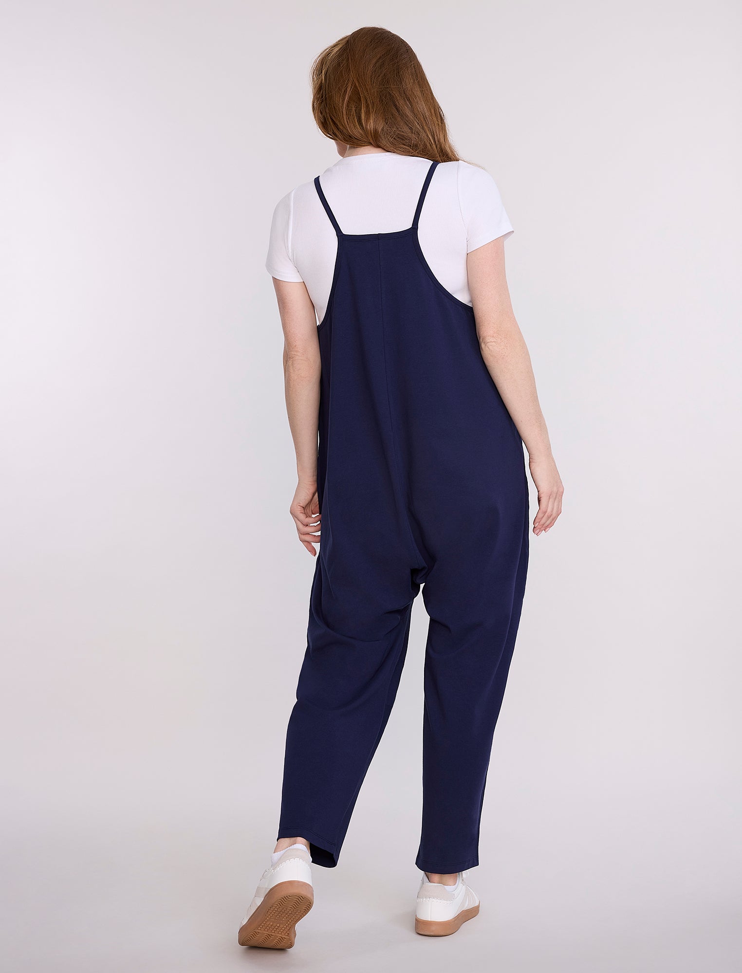 Pregnant woman wearing a navy blue jumpsuit over a white shirt on a light gray background